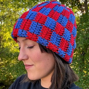 Könnte beinhalten: Handgehäkelte Mütze mit einem rot-blauen Schachbrettmuster. Die Mütze ist aus weichem Garn gefertigt und hat einen gerippten Bund. Ein stilvolles Accessoire für kaltes Wetter.