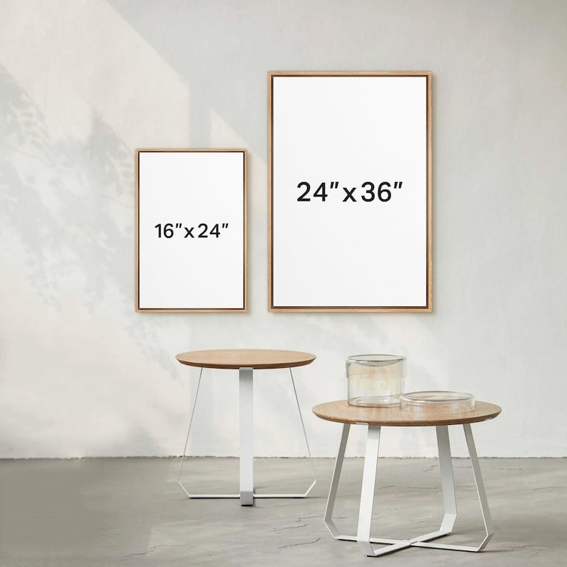 May include: Two wooden picture frames with white mats and black text indicating the size of each frame. The larger frame is 24" x 36" and the smaller frame is 16" x 24". Two white round tables with wooden tops are in the foreground.