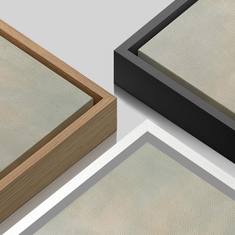 May include: Close-up of three canvas art pieces with different frame colors. One has a natural wood frame, another a black frame, and the third a white frame. The canvas has a neutral, light-colored surface.