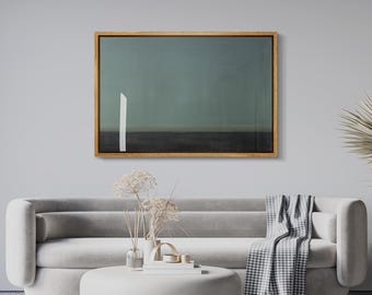 May include: A framed abstract art piece with a wooden frame. The artwork features a teal and dark gray background with a vertical white line. The art hangs above a gray sofa, a round coffee table, and a patterned rug.