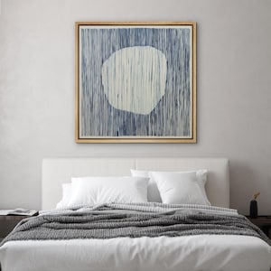 May include: Abstract wall art featuring a large, off-white, organic shape against a background of vertical blue lines. The artwork is framed in a natural wood tone and hangs above a bed with white bedding and a gray blanket.