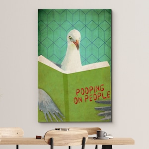 K&ouml;nnte beinhalten: Ein gr&uuml;nes Buch mit dem Text "POOPING ON PEOPLE" in roten Buchstaben. Eine wei&szlig;e M&ouml;we sitzt auf dem Buch und schaut den Betrachter an.