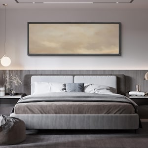 Puede incluir: Un dormitorio moderno con una cama grande, un cabecero tapizado gris y un edred&oacute;n de tonos neutros. Encima de la cama cuelga una obra de arte rectangular con un paisaje abstracto y apagado. La habitaci&oacute;n est&aacute; decorada con colores suaves y neutros.