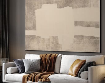 May include: A large abstract painting with a neutral color palette hangs above a white sofa. The artwork features beige and white rectangular shapes on a gray background. The sofa is adorned with pillows and a brown throw blanket.