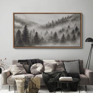 May include: A framed landscape art print depicts a misty forest scene. The artwork features a grayscale palette, with tall evergreen trees emerging from the fog. The rectangular frame is made of light brown wood, adding a natural touch to the artwork.