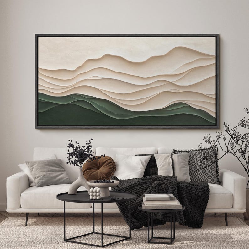 May include: A white couch with black throw blankets and pillows in a living room with a large abstract painting of beige and green waves hanging on the wall. There are two black coffee tables in front of the couch.