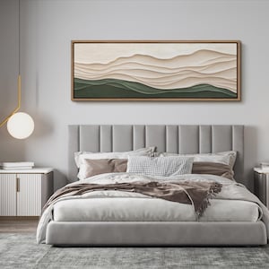 May include: A gray upholstered bed with a headboard featuring vertical panels. The bed has a white duvet and brown throw blanket. A long horizontal abstract painting with green and beige colors hangs above the bed.