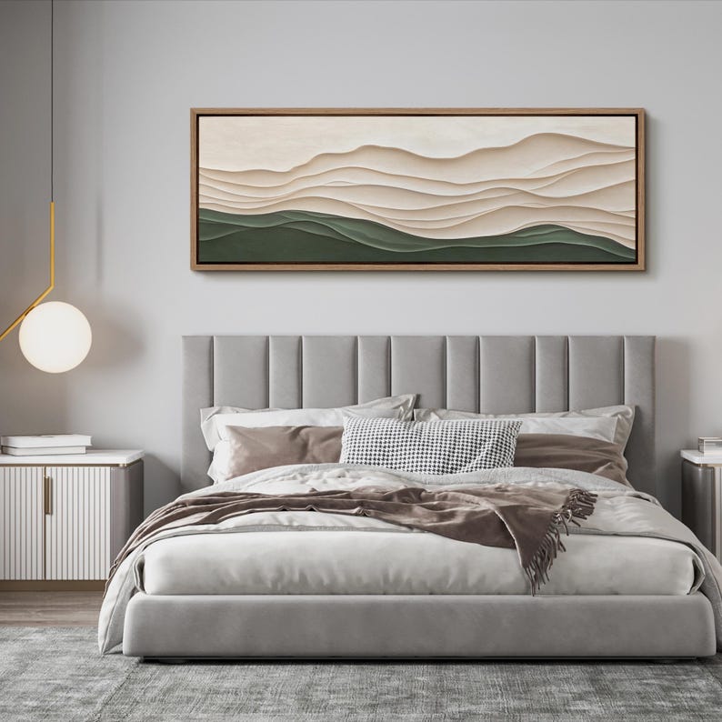 May include: A gray upholstered bed with a headboard featuring vertical panels. The bed has a white duvet and brown throw blanket. A long horizontal abstract painting with green and beige colors hangs above the bed.