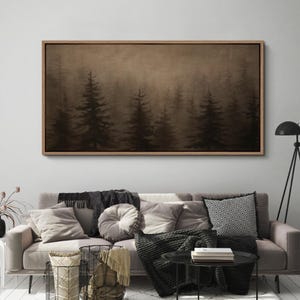May include: A framed canvas art piece depicting a misty forest scene. The artwork features silhouetted evergreen trees in varying sizes against a sepia-toned background. The frame is a light brown color, and the artwork is displayed above a sofa with pillows.
