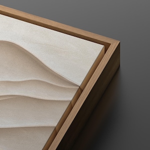 May include: A close-up of a framed canvas with a textured, beige surface that resembles sand dunes. The frame is made of natural wood.