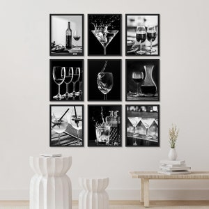 May include: A set of nine black and white framed prints featuring various images of wine glasses and cocktails. The prints are arranged in a grid pattern on a white wall.