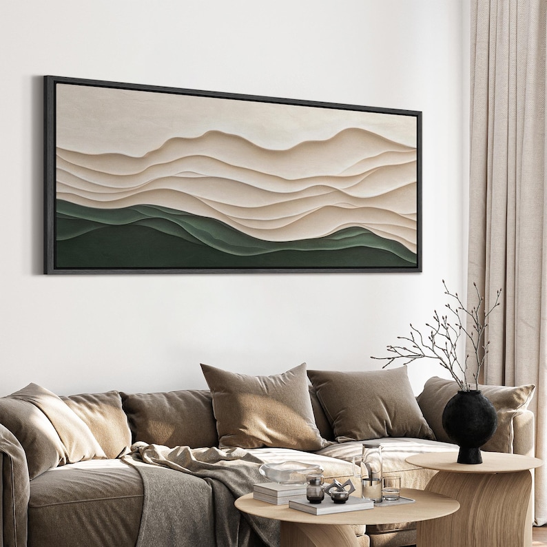 May include: Abstract wall art featuring a layered landscape with beige and green hues. The artwork is framed in black and hangs on a white wall above a brown couch.