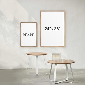 May include: Two framed canvases, one 16" x 24" and the other 24" x 36", with light wood frames. Two small round tables with light wood tops and white metal geometric legs are in the foreground. A glass jar and a clear dish sit on one table.
