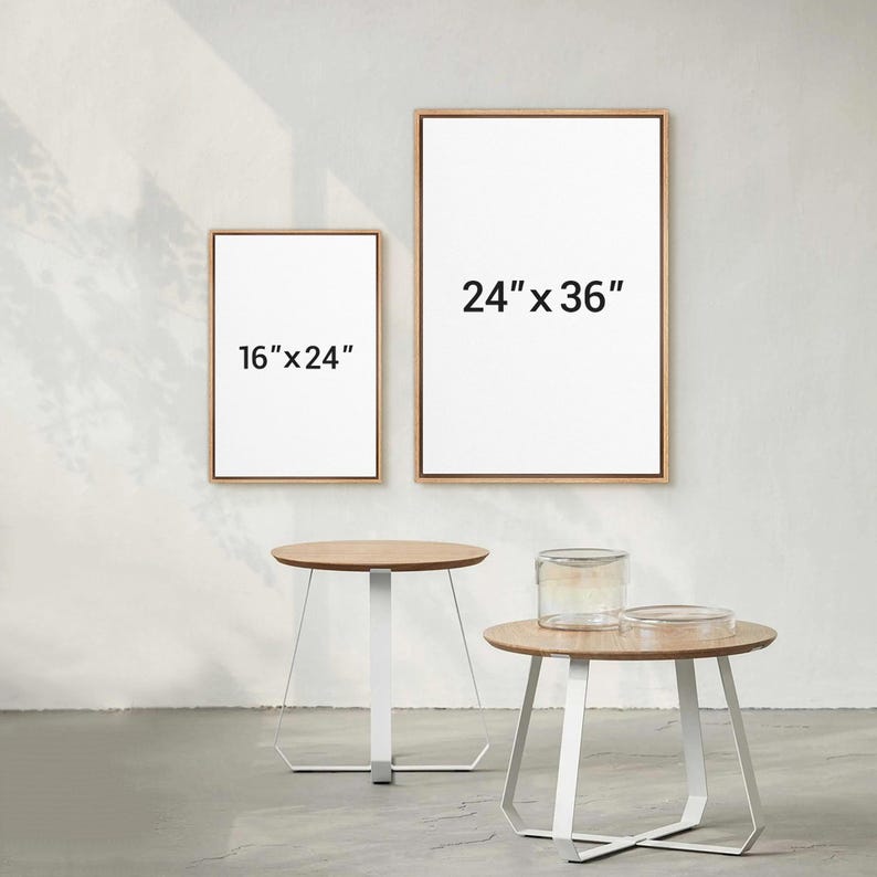 May include: Two framed canvases, one 16" x 24" and the other 24" x 36", with light wood frames. Two small round tables with light wood tops and white metal geometric legs are in the foreground. A glass jar and a clear dish sit on one table.