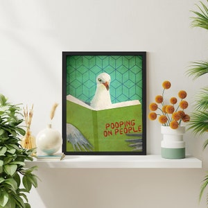 K&ouml;nnte beinhalten: Ein gerahmter Druck einer M&ouml;we, die ein Buch mit dem Titel "Pooping on People" liest. Das Buch ist gr&uuml;n und die M&ouml;we ist wei&szlig;. Der Hintergrund ist ein t&uuml;rkisfarbenes und gr&uuml;nes geometrisches Muster.