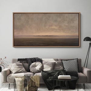 May include: A framed landscape painting with a muted color palette of browns, tans, and grays. The artwork depicts a serene, expansive view of a field or marsh under a cloudy sky. The wooden frame adds a touch of warmth to the piece.