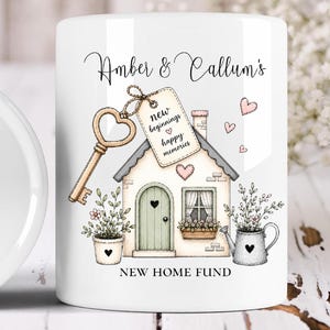 Puede incluir: Una taza de cerámica blanca con una ilustración impresa de una casa con puerta verde, una llave y plantas en macetas. El texto dice Amber & Callum's, new beginnings happy memories y NEW HOME FUND. Pequeños corazones rosas rodean la casa.