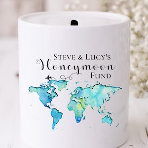 Pode incluir: Jarro de dinheiro de cerâmica branca com um design de mapa do mundo em aquarela azul e verde. O texto "STEVE & LUCY'S Honeymoon FUND" está impresso no jarro.