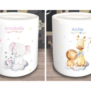 Könnte beinhalten: Zwei weiße Keramik-Sparschweine mit personalisierten Namen, Annabelle und Archie. Das Sparschwein mit Annabelle hat einen rosa Elefanten und einen Pandabären auf einer Wolke. Das Sparschwein mit Archie hat eine Giraffe und einen Löwen auf einer Wolke.