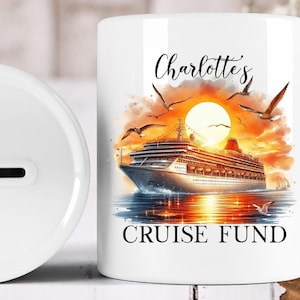 May include: White ceramic money bank with a cruise ship design. The design features a cruise ship on the water with a sunset in the background, seagulls, and the words "Charlotte's Cruise Fund."