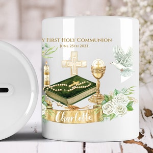 Può includere: Salvadanaio in ceramica bianca con un design oro e verde. Il design include una croce, una colomba, un calice, una bibbia e un rosario. Il testo sulla scatola recita "My First Holy Communion June 25th 2023 Charlotte".