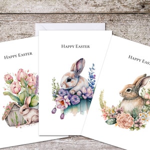 May include: Three watercolour Easter cards featuring bunnies and flowers. The first card has a bunny sitting in a flower pot with pink tulips. The second card has a bunny sitting in a flower pot with purple flowers. The third card has a bunny sitting in a wreath of flowers.