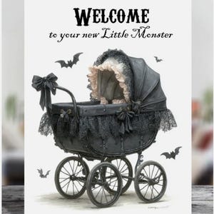 May include: A greeting card with the text "WELCOME to your new Little Monster". The card features a black baby carriage with lace trim and bows, and bat illustrations. The carriage has four spoked wheels.
