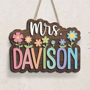 May include: A wooden sign with the text "mrs. DAVISON" in colorful letters. The sign is decorated with flowers in pink, yellow, blue, and green.