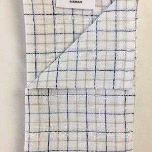May include: A white kitchen towel with a blue and tan plaid pattern. The towel is folded in half and has a label that reads "Rip Snorters Handmade".