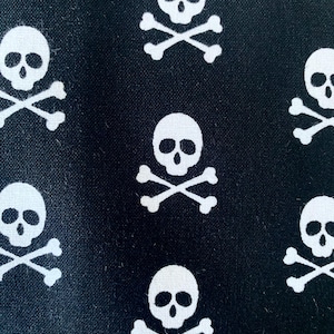 Könnte beinhalten: Schwarzer Stoff mit einem sich wiederholenden Muster aus weißen Totenköpfen und gekreuzten Knochen.