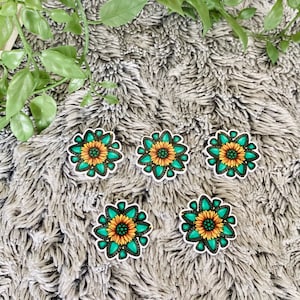 May include: Five turquoise and yellow sunflower stickers on a gray fuzzy surface.