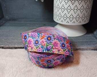 Può includere: Due bobine di nastro di raso rosa con una stampa floreale con fiori viola, rosa e verdi. Il nastro è arrotolato e posto su una superficie bianca e soffice.
