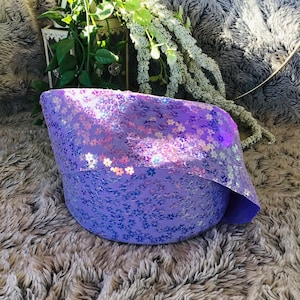 May include: A purple sequined fabric with a floral pattern. The fabric is folded and sitting on a fluffy gray surface.