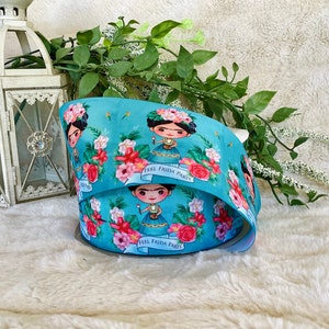May include: Blue ribbon with a repeating pattern of a cartoon Frida Kahlo wearing a flower crown and holding a paintbrush. The ribbon has the text "Feel Frida Party" printed on it.