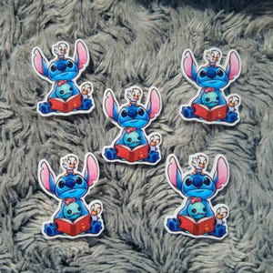 May include: Five die-cut stickers featuring the blue alien Stitch from Lilo & Stitch. Each sticker shows Stitch reading a red book, with a small bird on his head and two smaller Stitch figures. The stickers have a white border.