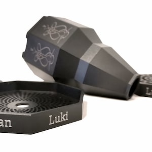 May include: A black metal hookah bowl with a hexagonal base and a decorative design. The bowl is engraved with the words "Luki Paze" and "Ryan".