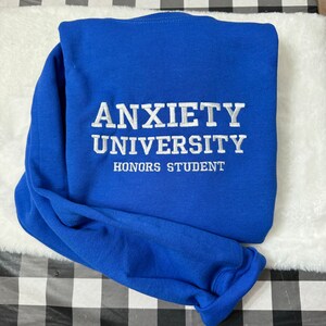 May include: A royal blue sweatshirt with white embroidered text that reads "Anxiety University Honors Student".