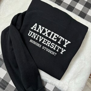 May include: Black sweatshirt with white embroidered text that reads "Anxiety University Honors Student".