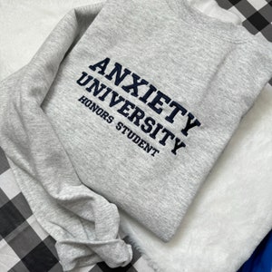 May include: A gray sweatshirt with the text "Anxiety University Honors Student" embroidered in navy blue.
