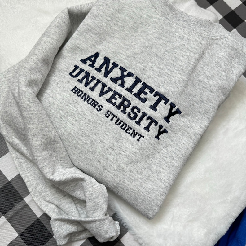 May include: A gray sweatshirt with the text "Anxiety University Honors Student" embroidered in navy blue.