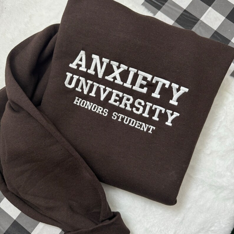 May include: A brown sweatshirt with the text "Anxiety University Honors Student" embroidered in white.