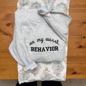Può includere: Felpa grigia con il testo "on my worst behavior" ricamato in nero.