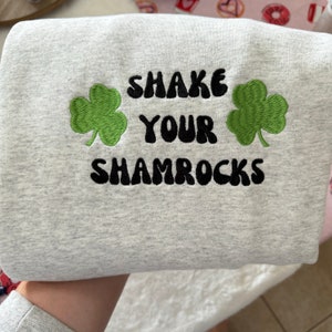 May include: Gray sweatshirt with the text "Shake Your Shamrocks" in black with two green shamrock designs on either side of the text.