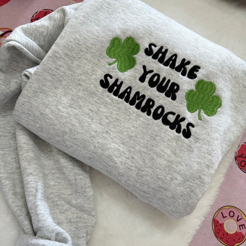 May include: Gray sweatshirt with black embroidered text that says "Shake Your Shamrocks" and two green shamrock designs.