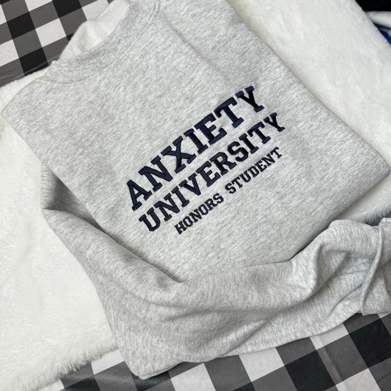 May include: A gray sweatshirt with the text "Anxiety University Honors Student" embroidered in navy blue.