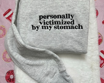 May include: Gray sweatshirt with black embroidered text that reads "personally victimized by my stomach".