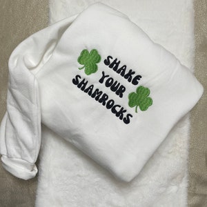 May include: White sweatshirt with green shamrock embroidery and the text "Shake Your Shamrocks" in black.