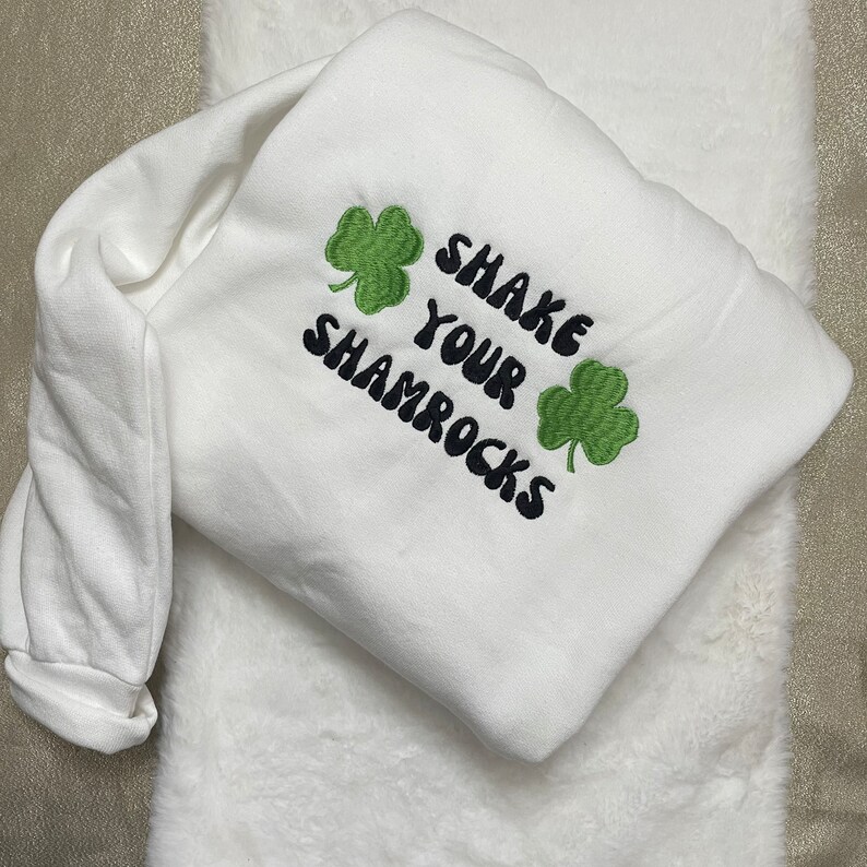 May include: White sweatshirt with green shamrock embroidery and the text "Shake Your Shamrocks" in black.