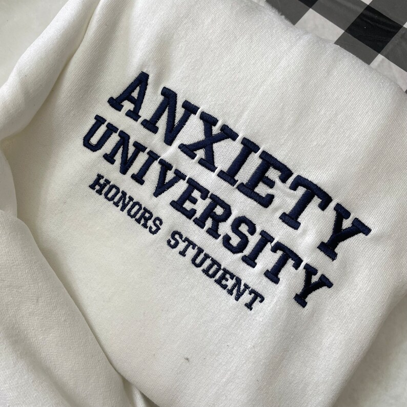 White sweatshirt with Anxiety University Honors Student embroidered in black thread.