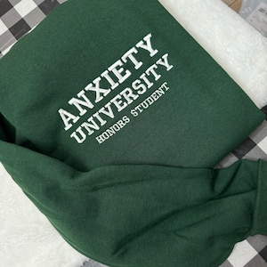 May include: A dark green sweatshirt with the text "ANXIETY UNIVERSITY HONORS STUDENT" embroidered in white.